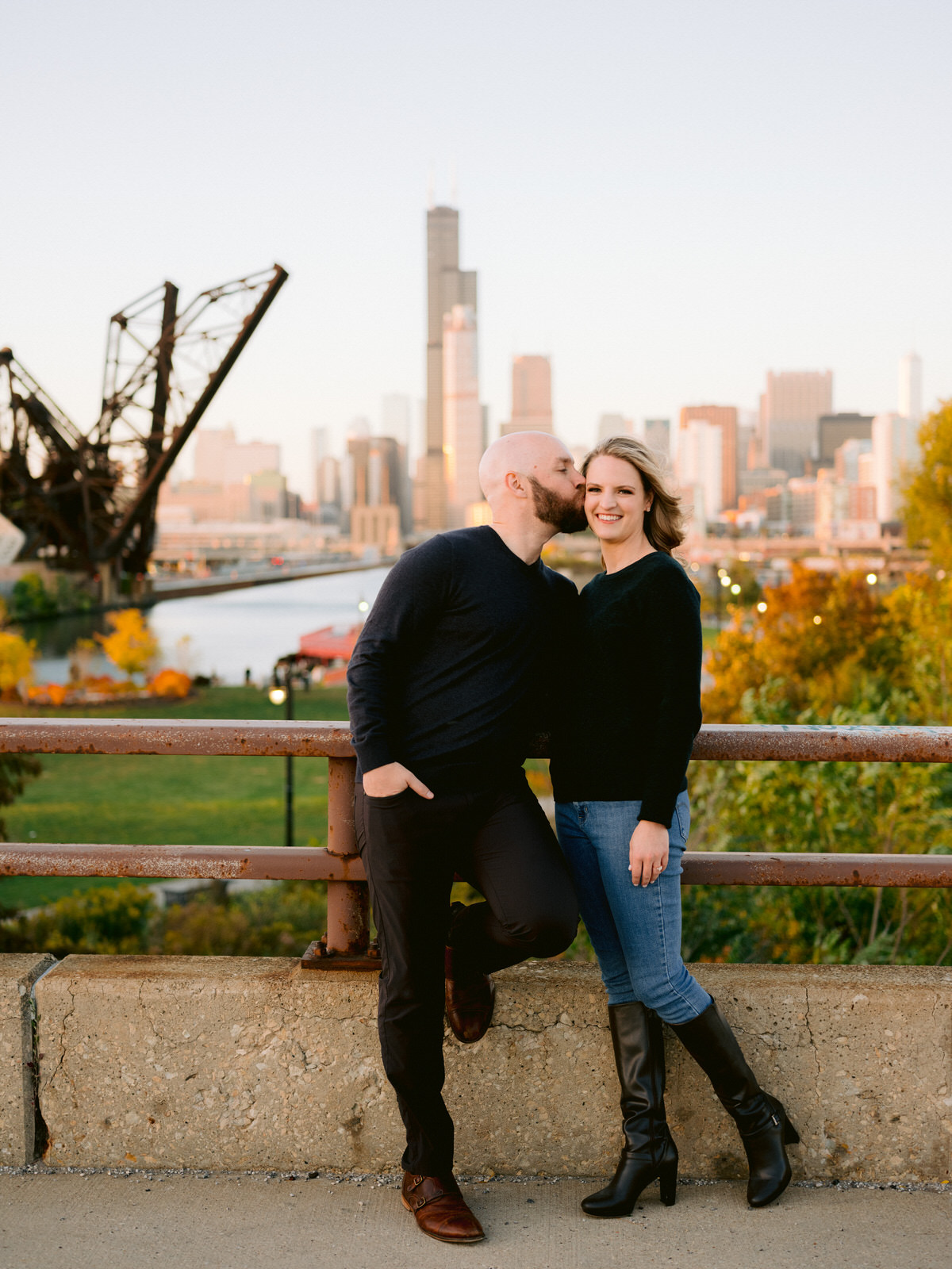 ping tom memorial park engagement photos guy kissing girl's cheek looking over the Chicago skyline and Chinatown bridge