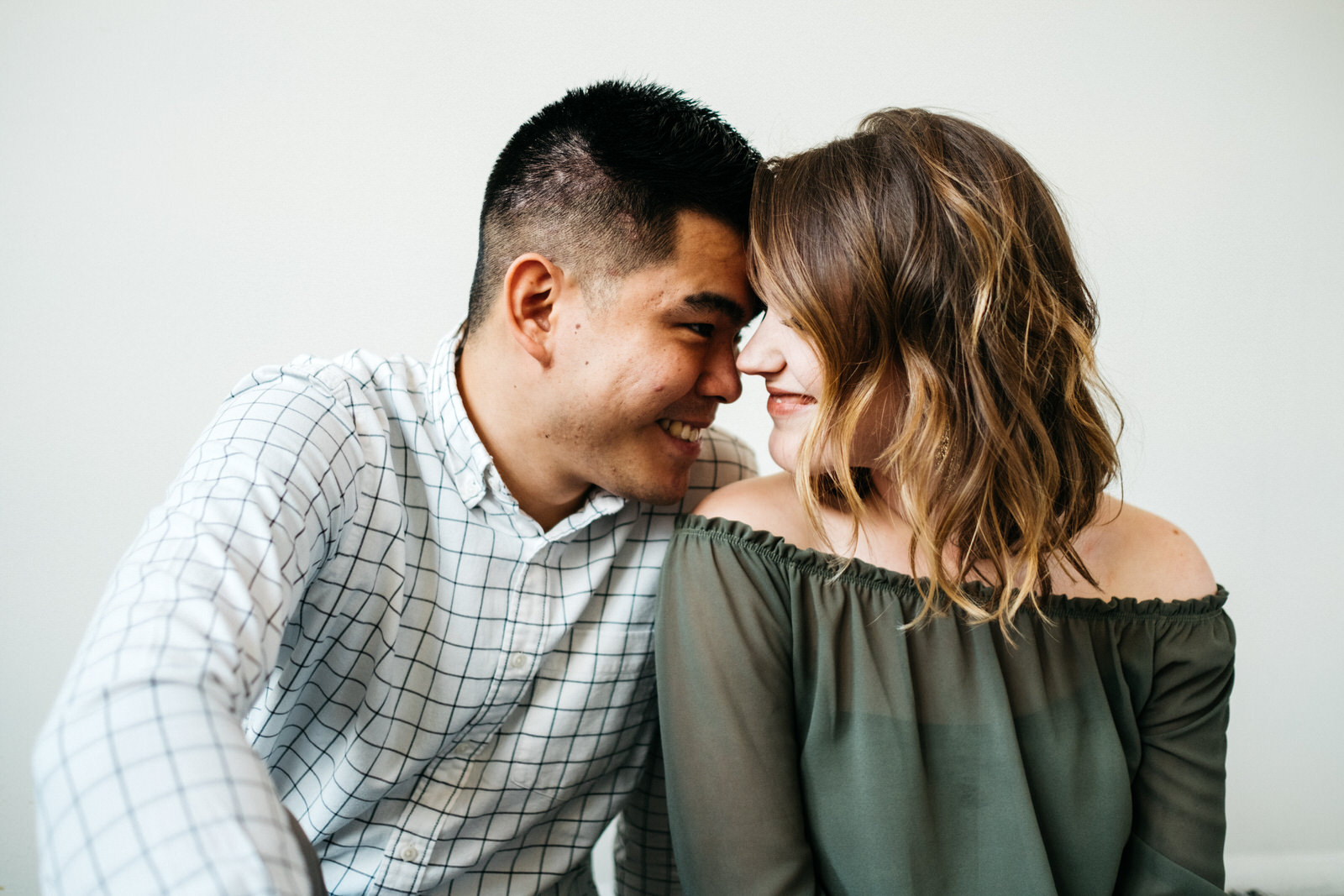 Couple cuddling in front of white backdrop at Creative Club Chicago for Chicago engagement session locations. Wedding photography by Michael & Kristin Photo and Video