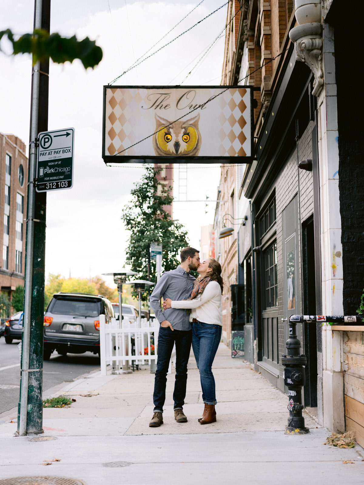 Couple stands in front of The Owl, a Chicago bar, for Chicago engagement session locations. Photography by Michael & Kristin Photo and Video