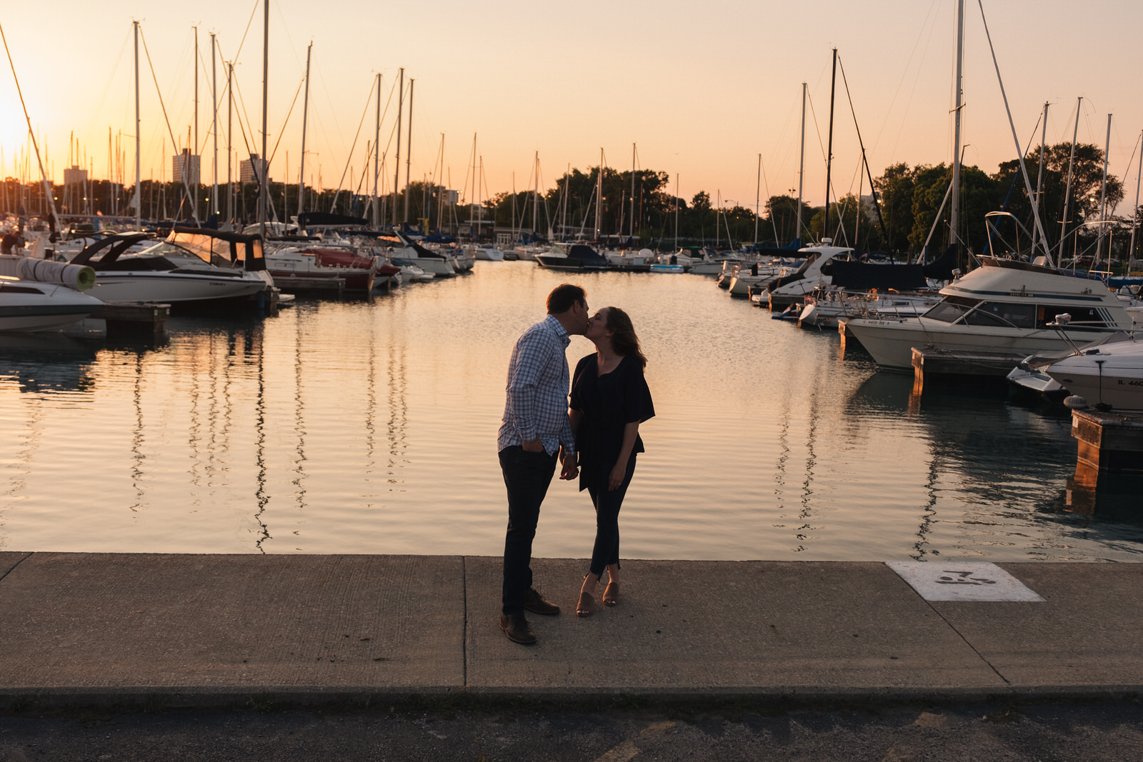 Couple stands in front of boats docked at Montrose Harbor for Chicago engagement session locations. Photography by Michael and Kristin Photo and Video
